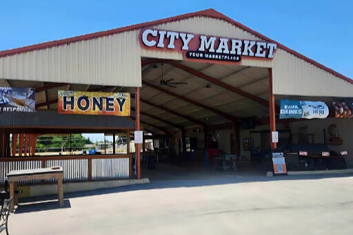 Front entrance of City Market in Richland Hills, Texas, where Levi's Lunchbox is located. The building features a red-trimmed metal roof with signs for honey and drinks.